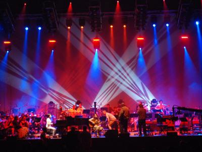 Musical ensemble performing a wide variety of instruments on a colorfully lit stage