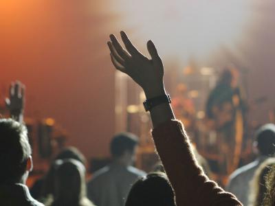 Audience member with their hands up at a concert in front of the band on stage
