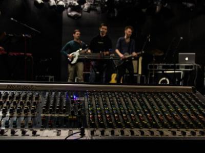 Band in a recording session from a point of view behind the mixing console